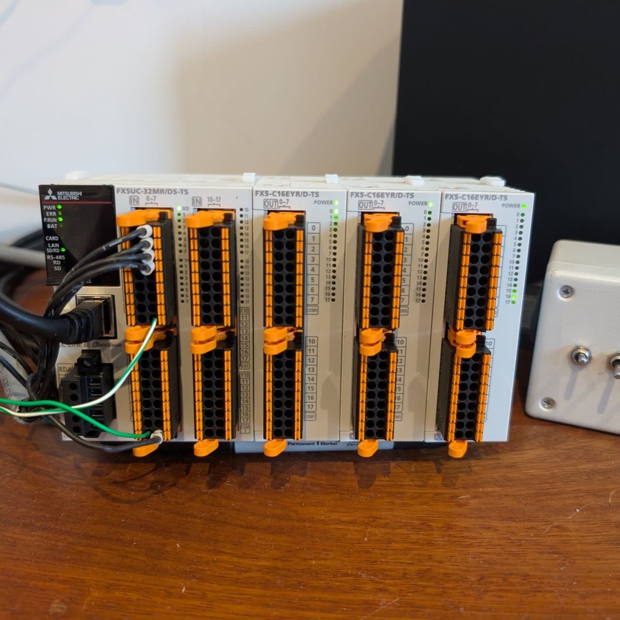 Mitsubishi FX5UC PLC with three 16-point output modules and orange spring clamp connectors, wired up for bench testing