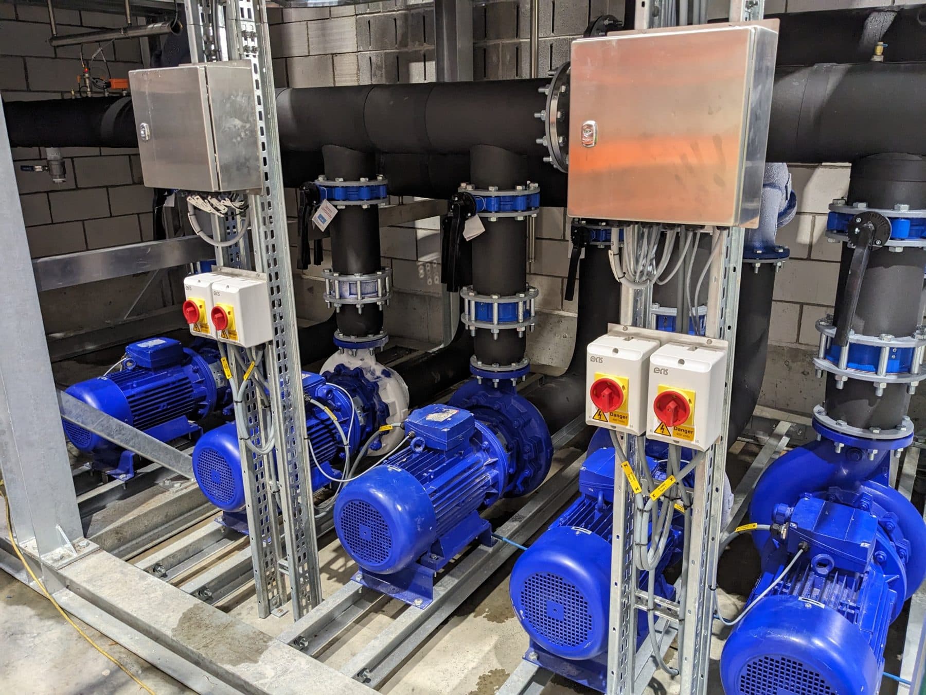 Row of blue chilled water pumps with local isolators and insulated pipework in a plant room