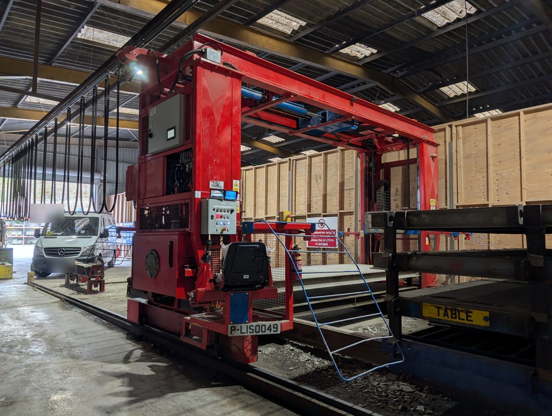 Red rail-mounted precast concrete handling machine in a production shed