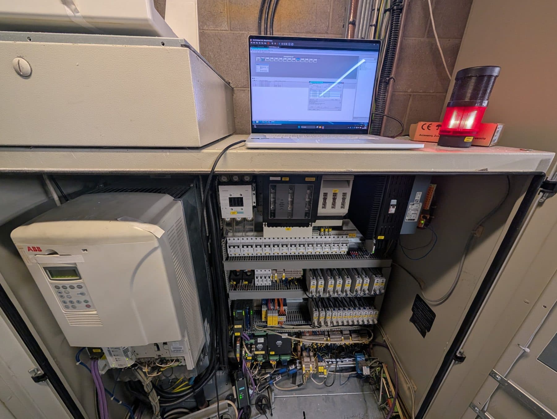 Laptop connected to a PLC on top of an open control panel during fault-finding, with an ABB drive inside
